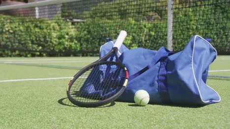 Blue-sports-bag,-tennis-racket-and-ball-on-tennis-court-on-sunny-day