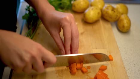 female hands cutting a carrot on a wooden cutting board with parsley and potatoes in the background