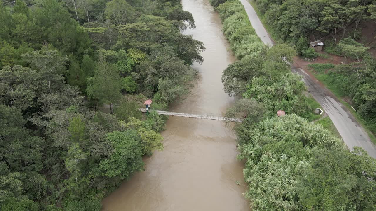 sobrevuelo aéreo de carretera estrecha y puente peatonal sobre el río, selva peruana