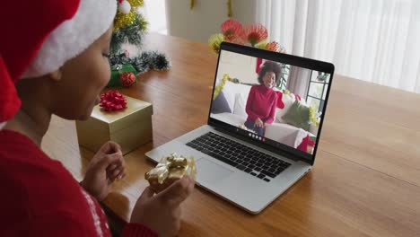 Mujer-Afroamericana-Con-Gorro-De-Papá-Noel-Usando-Una-Computadora-Portátil-Para-Una-Videollamada-Navideña,-Con-Un-Amigo-En-La-Pantalla