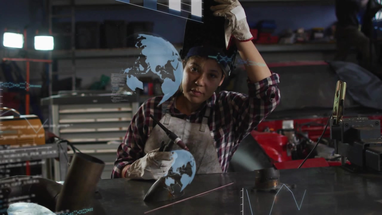 Female welder holding torch, lifting helmet and inspecting weld while holo charts overlaying work