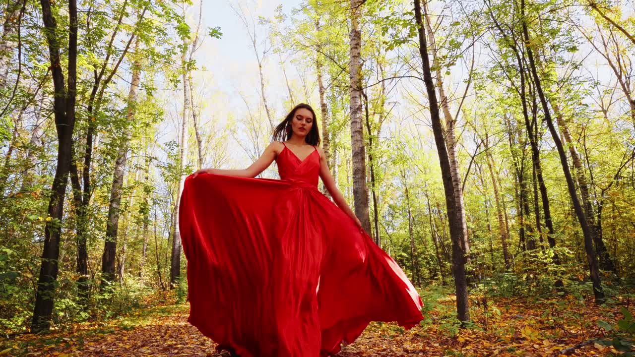 A Captivating Model in a Flowing Red Dress Graces a Serene Forest Landscape, Surrounded by Vibrant Autumn Colors and Towering Trees, Evoking Beauty and Elegance