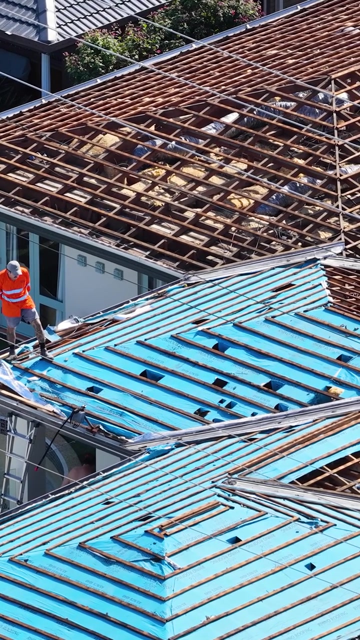 Aerial view of workers installing blue protective tarp on a residential roof under renovation.