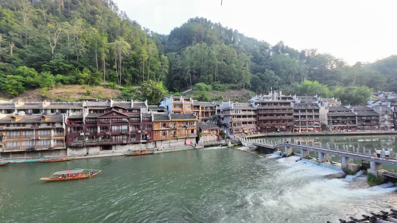 Time lapse of wooden boats moving along the Tuojiang River in Fenghuang Old Town, Hunan, with stilt houses and traditional Chinese architecture by the water