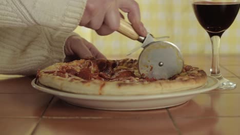 hand cutting pepperoni pizza with pizza wheel medium shot