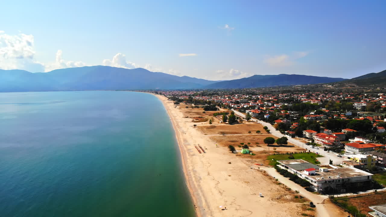Panorama of the Asprovalta with multiple buildings and greenery, green hills on the background. Aegean sea coast. Long beach along the town. Sunny day. Greece