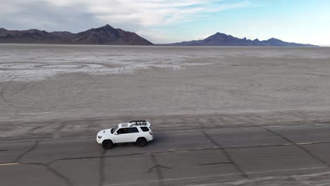 tracking drone shot of white suv vehicle on asphalt road by bonneville salt flats, utah usa