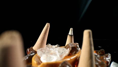 static view of unlit incense cones in a decorative rock garden which shakes as off camera hand is trying to direct smoke, finger pushes over lit cone - smoke is more visible