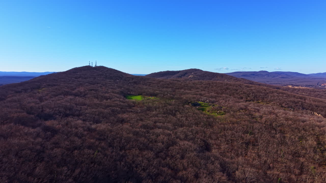 View of a forested mountain area with high towers against a clear blue sky in a rural landscape during daylight hours