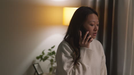 anxious or stressed woman spending evening at home walking around lounge talking on mobile phone 1