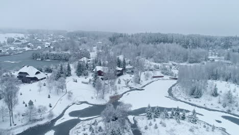 snow covered houses in winter forest background - aerial drone shot