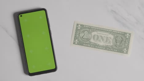 overhead currency shot of hand putting down us 1 dollar bill next to green screen mobile phone