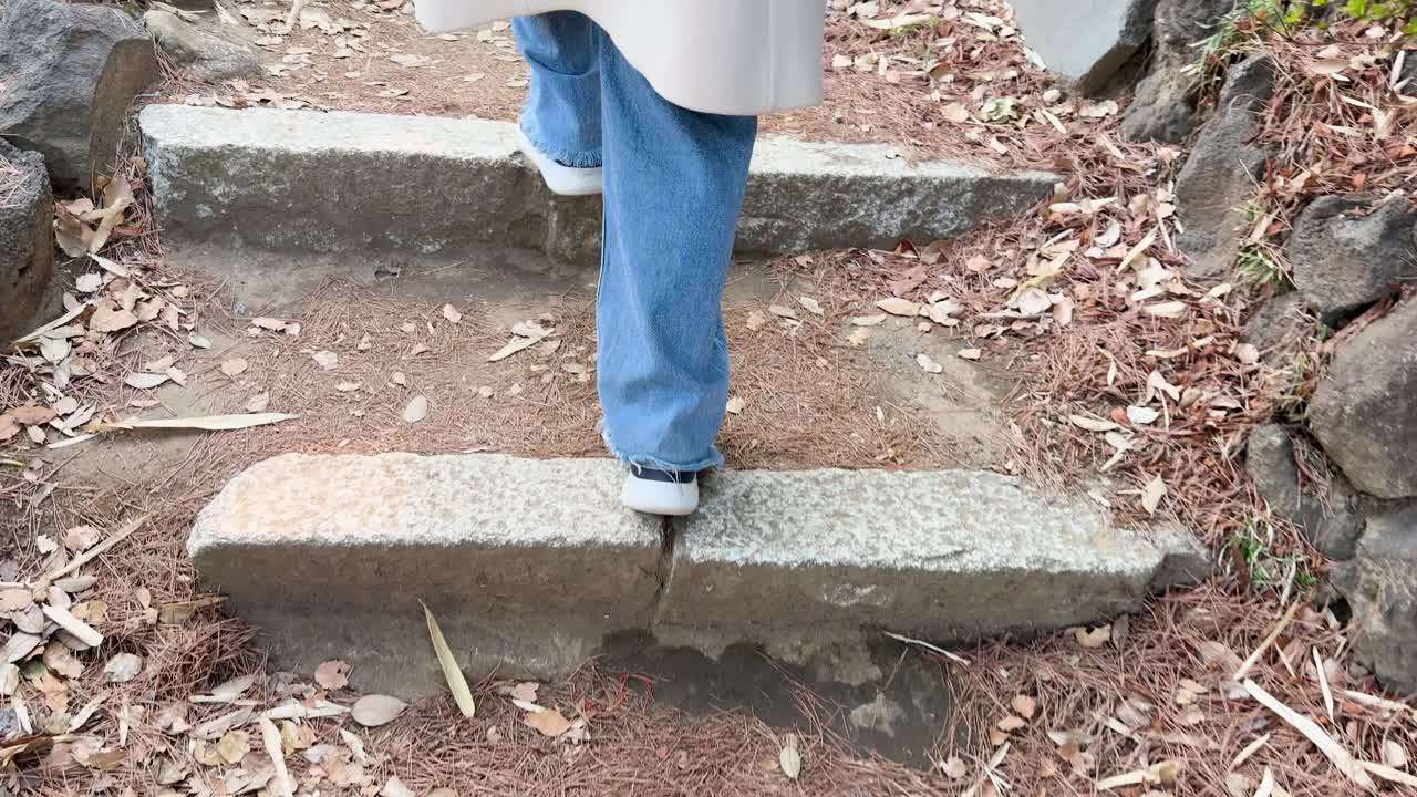 Low angle shot of a woman walking up rustic stone steps in a Japanese garden