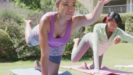 Happy-biracial-sisters-doing-yoga-and-stretching-in-garden,-in-slow-motion