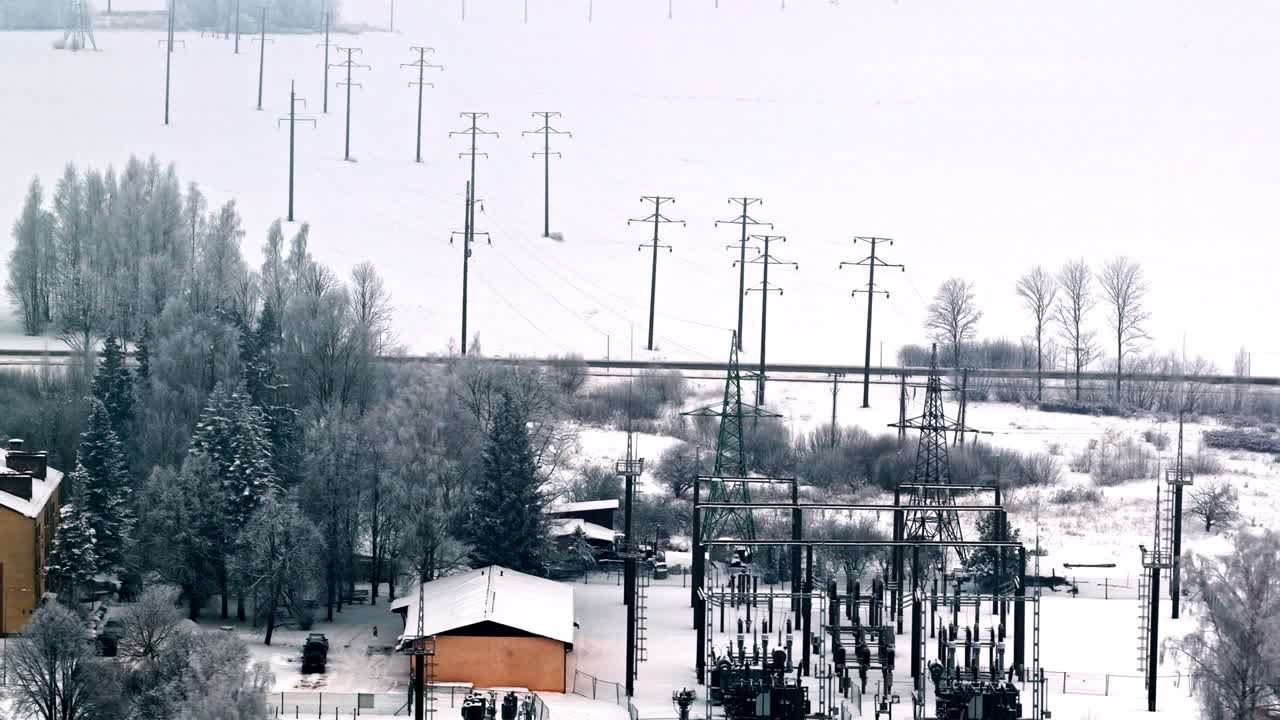 Hoher Winkel einer Stromverteilungsstation und Hochspannungsleitungen mit Übertragungstürmen in einem gefrorenen Winterfeld an einem kalten Tag in Jelgava, Lettland