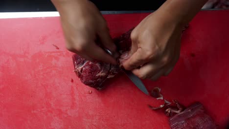 close up top view of two hands cutting and preparing a piece of meat with a chef knife