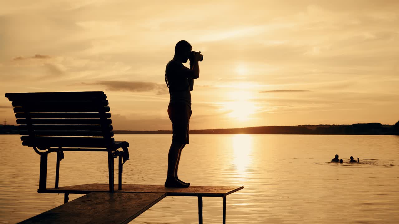 Photographer taking picture of landscape during sunset. Silhouette of people swimming in the river at sunset
