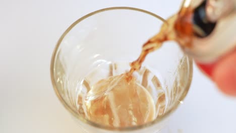 pouring cola into glass with ice cubes on white background