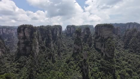 slow pan right reveals towering vertical cliffs covered with dense green forest under cloudy sky
