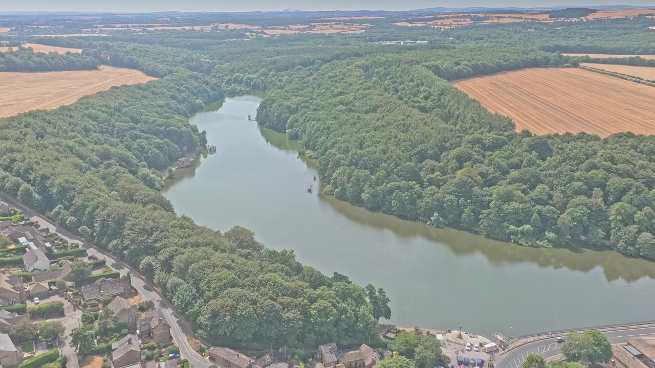 Il lago di Newmillerdam si snoda attraverso un fitto bosco accanto a terreni agricoli e case del villaggio vicino a Newmillerdam, Wakefield, West Yorkshire, Inghilterra, Europa, ripresa aerea con drone in avanti