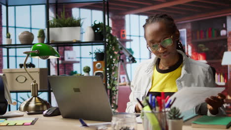 freelancer at home checking data on laptop, comparing with paperwork files