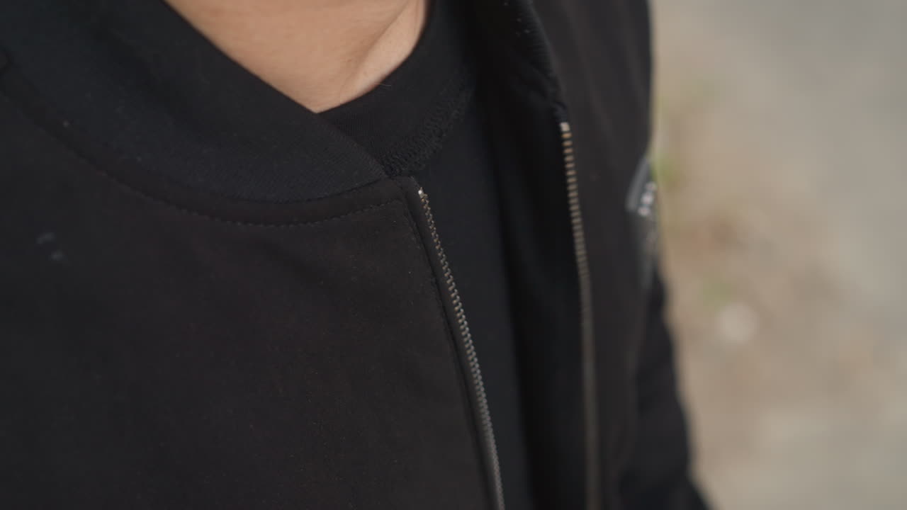 primer plano de un hombre ajustando la cremallera de una chaqueta de exterior, toma detallada de un hombre arreglando la chaqueta con luz natural, perspectiva cercana que captura los movimientos deliberados mientras ajusta la cremallera en la ropa de exterior