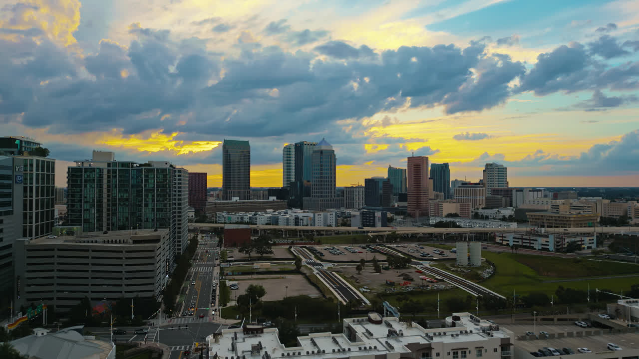 Aerial view of the downtown Tampa city skyline and city blocks as people drive along the street and highways at dusk with a golden yellow sky and blue clouds
