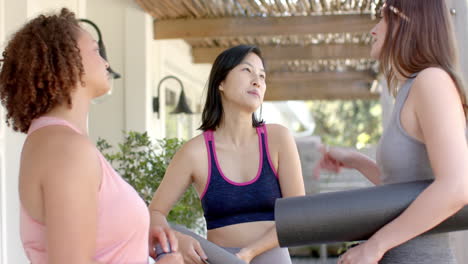 exercising together, three diverse women friends holding yoga mats and chatting outdoors