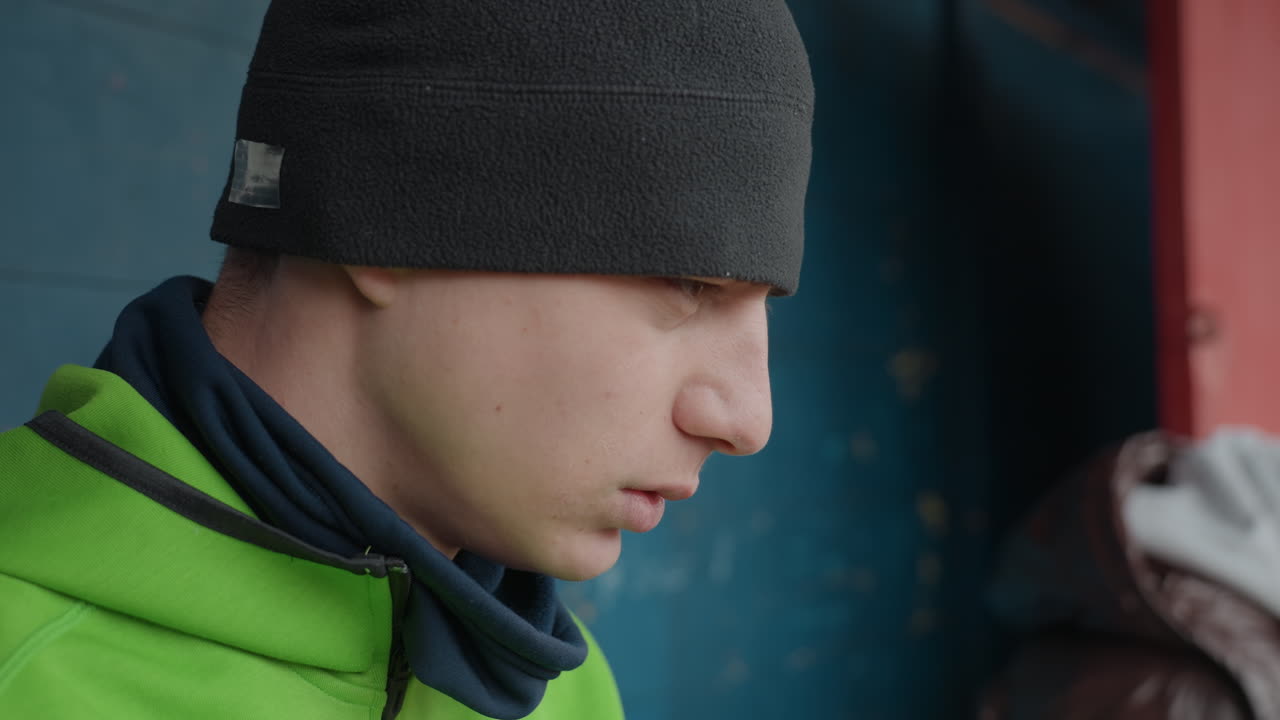 경기에서 주의 깊게 듣고 있는 남자의 클로즈업, 더그아웃에서 스카프와 비니를 쓴 채 집중하고 있는 남자의 모습, 벤치 구역에서 전술 토론 중에 주의 깊게 집중하고 있는 남성 운동선수의 초상화