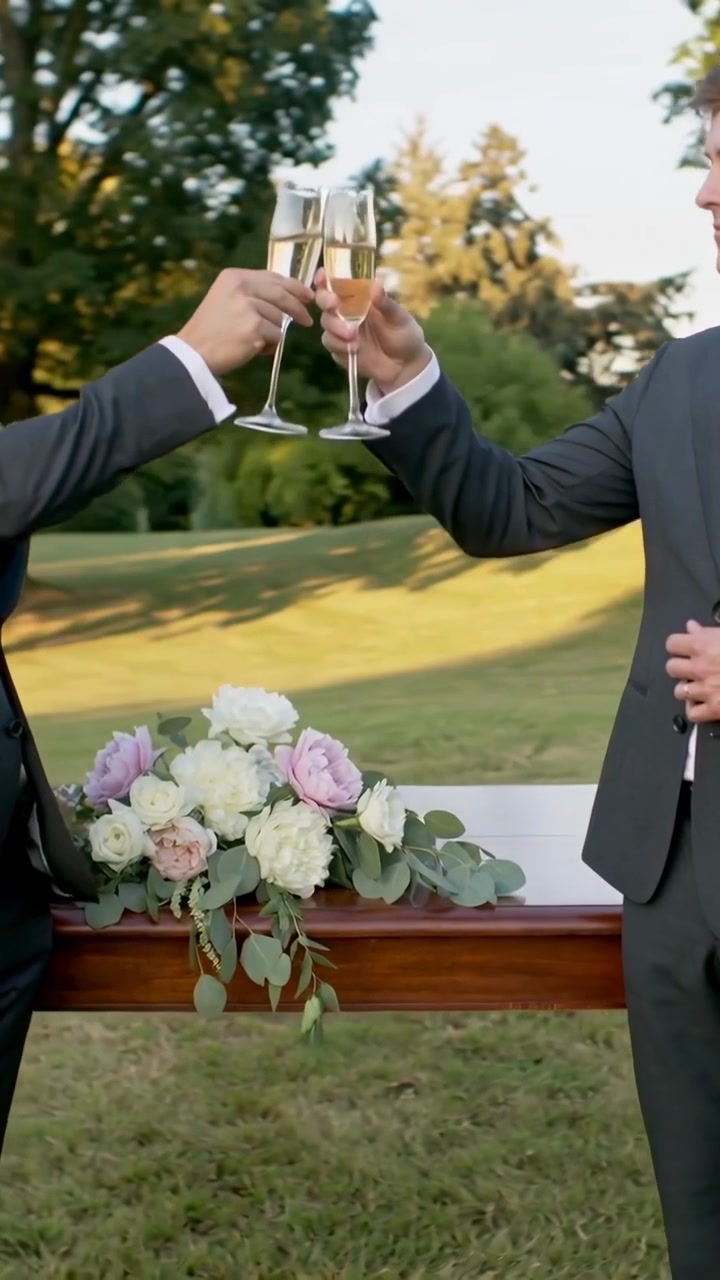 Due uomini alzano i calici di champagne, dando inizio a un brindisi nuziale su un tavolo con fiori che segnano la celebrazione.
