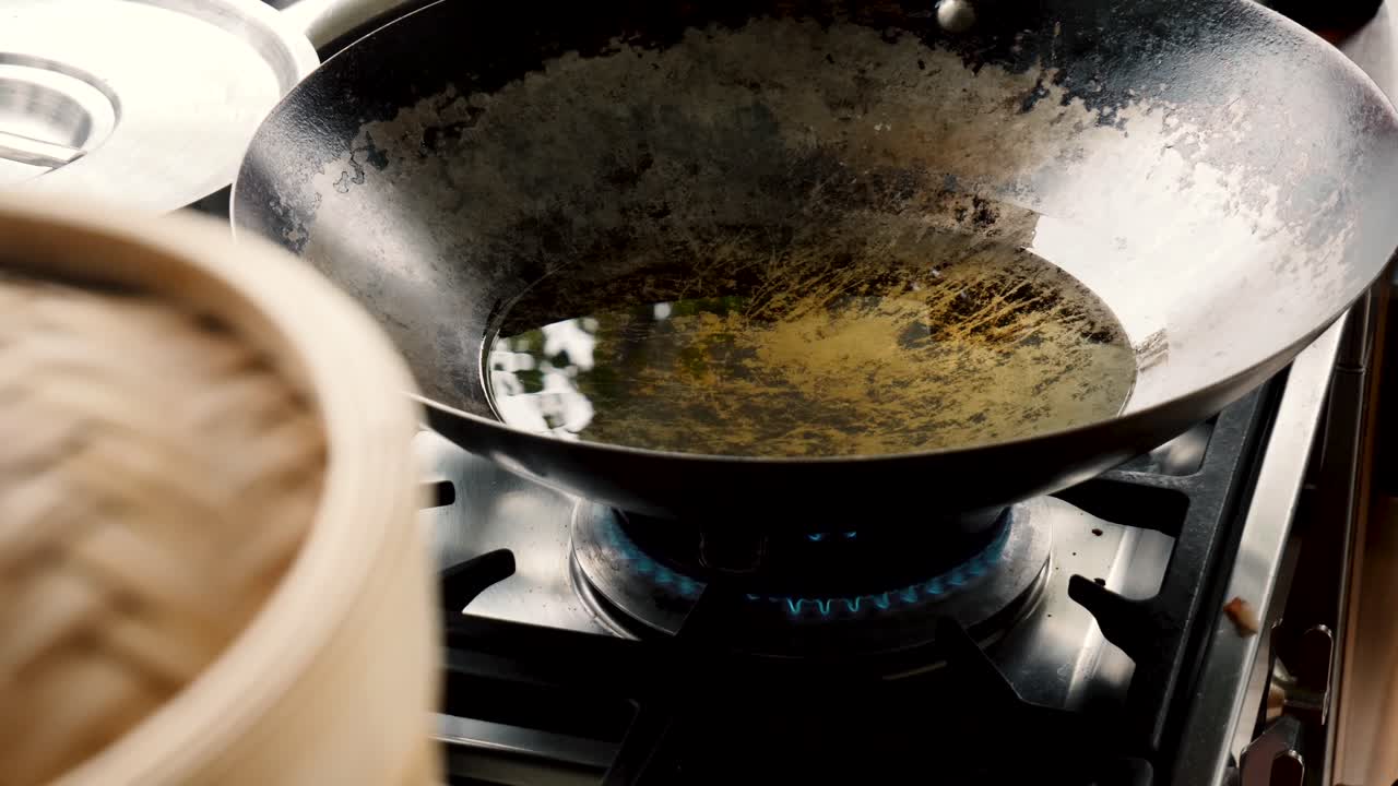Clear liquid grease heats up in metal wok on blue gas flame stove top, close up static