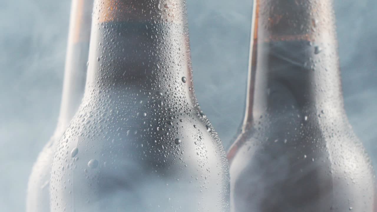 Three very cold beer bottles and smoke rotating on black background. Close up