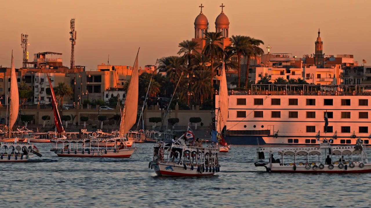 Una vista dettagliata con teleobiettivo mette in risalto la silhouette dello skyline di Luxor lungo la sponda orientale del fiume Nilo al tramonto.