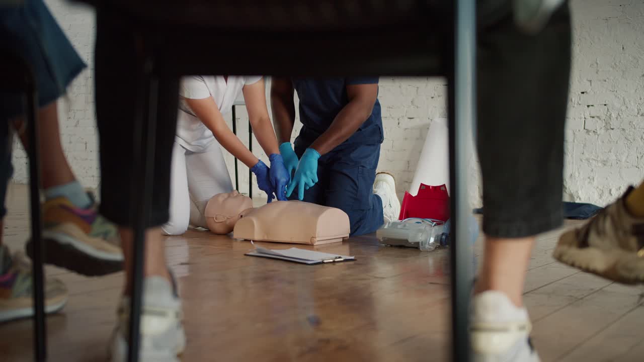 아래쪽: 파란 유니폼을 입은 흑인 남성 의사와 그의 보좌관,  유니폼를 입은 여성 간호사가 인공 호흡 훈련을 수행합니다.