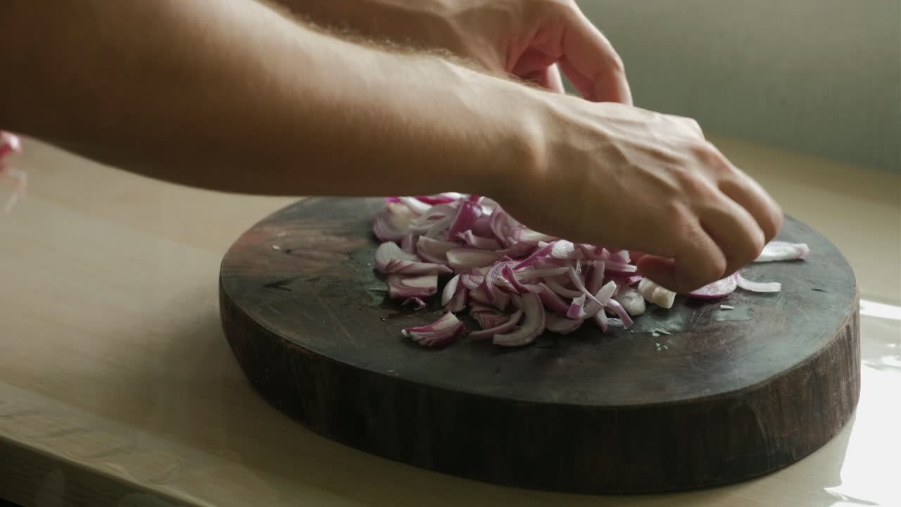 Close-up shot of hands separating and segregating thinly slice red onions on wooden chopping board.