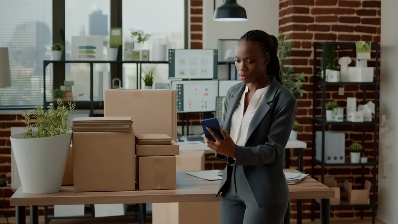 Donna Afroamericana che Lavora con Pacchi e Smartphone in un Ufficio
