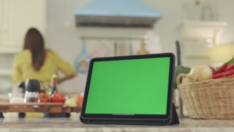 tableta con una pantalla verde con un hermoso fondo cocinando en la casa con una cara feliz, la esposa hace el desayuno felizmente en su casa.