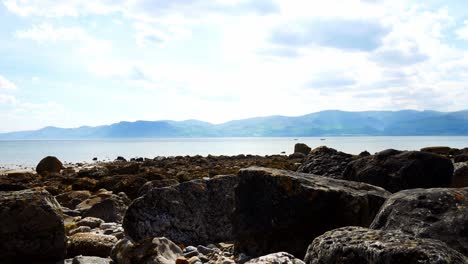 Colourful-variety-of-stone-boulders-beach-landscape-under-North-Wales-mountain-range-forward-dolly-left