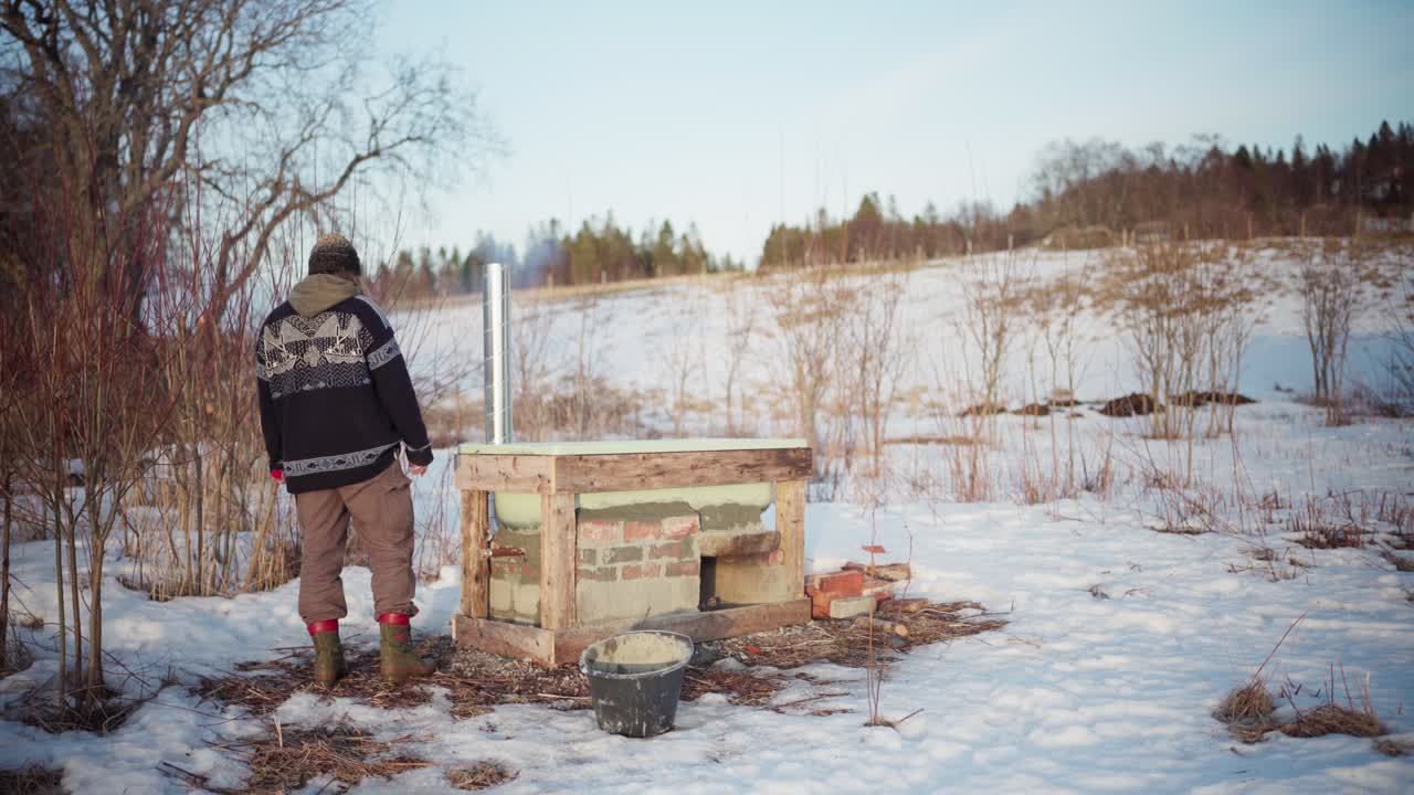 hombre construyendo una bañera de baño caliente fuera de su cabaña en invierno