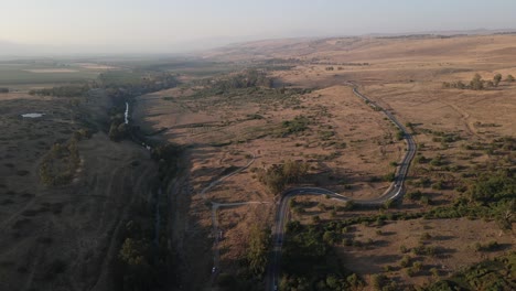 curved road cutting through countryside next to jordan river, israel, drone view