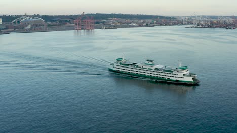 Toma-Aérea-De-Un-Ferry-Del-Estado-De-Washington-Que-Se-Dirige-A-La-Isla-De-Bainbridge-Con-El-Distrito-Del-Estadio-Al-Fondo