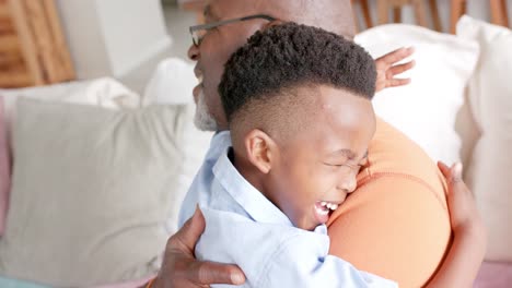 feliz nieto afroamericano y abuelo abrazando y sonriendo en el sofá en casa, cámara lenta