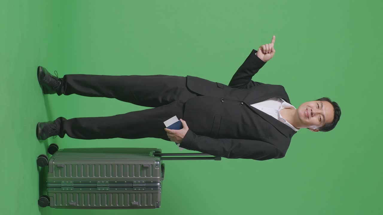 짐과 여권으로 가득 찬 아시아 사업가 여행자의 몸은 녹색 스크린 배경 스튜디오에 서있는 동안 웃고 을 가리키고 있습니다.