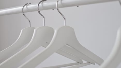 woman's hand picks up white empty wooden hanger from rack against white wall. concept of sale in the store, discounts, minimalistic advertising. fashion, stylish metal hook hangers. equipment for home