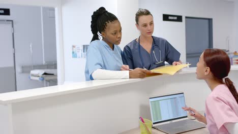 diverse doctors talking to medical recepcionist sitting at front desk at hospital, slow motion