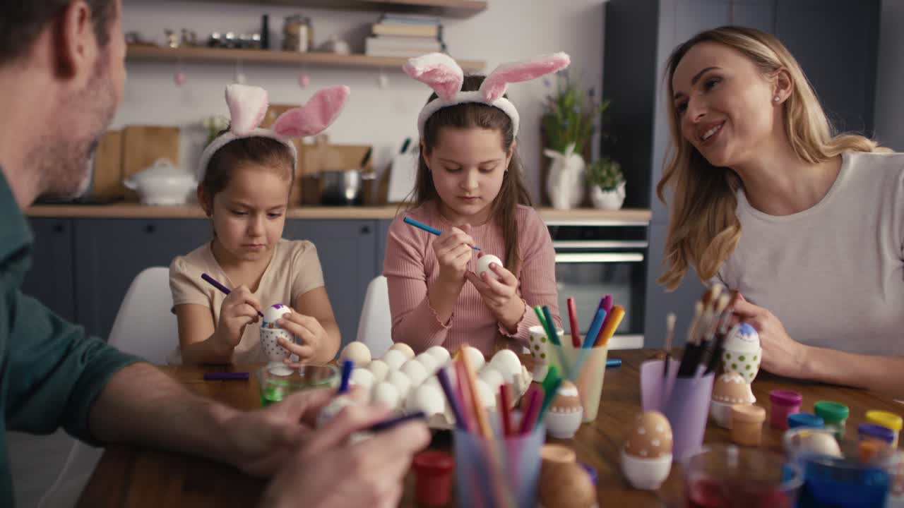 una famiglia caucasica di quattro persone che chiacchiera e decora le uova di pasqua a casa.