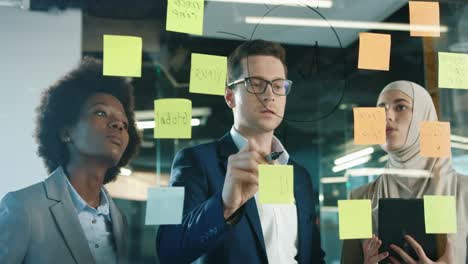 close up view of multiethnic business people group working in a modern office while writing on glass in a cabinet with sticky notes