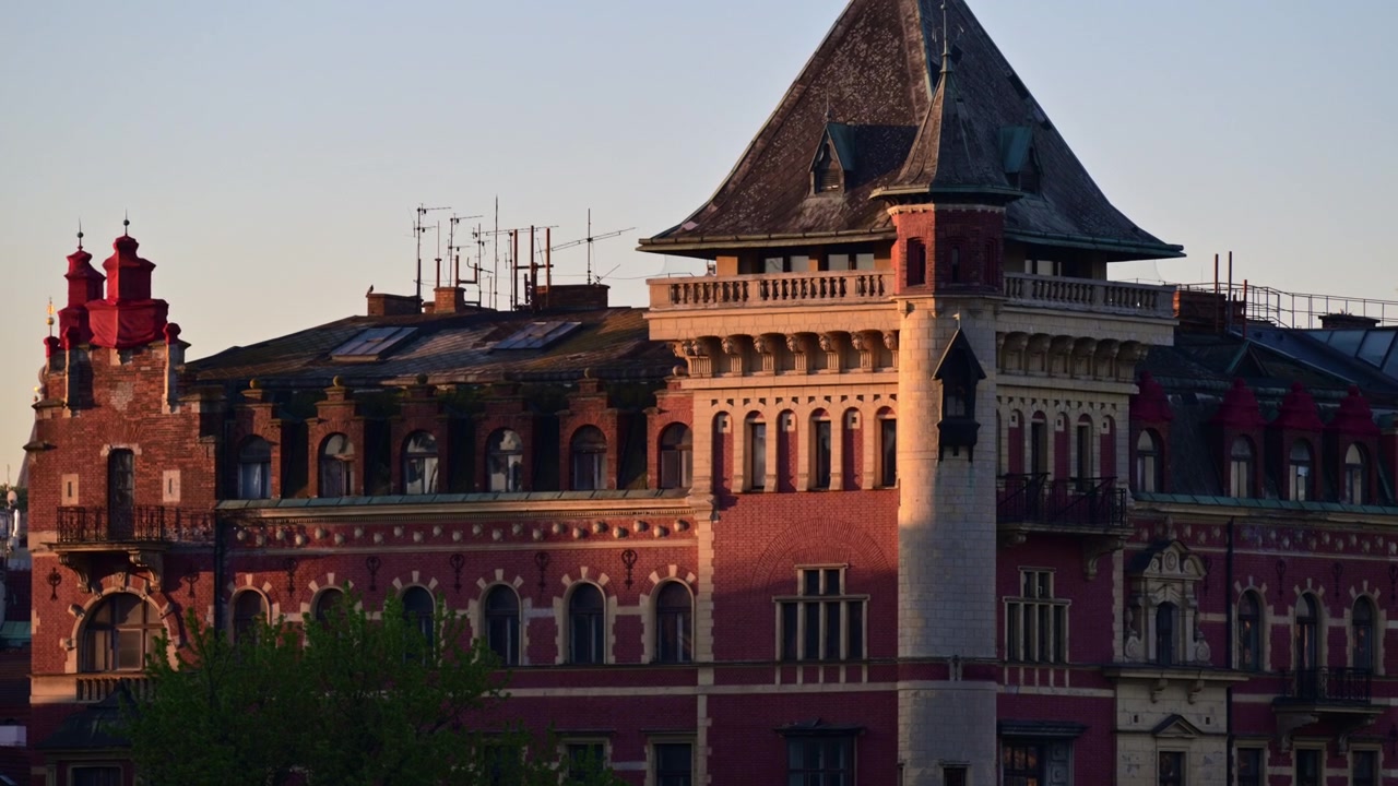 Um edifício de tijolos vermelhos com uma torre de canto e telhado íngreme de ardósia sob a luz do início da manhã, Praga, República Checa