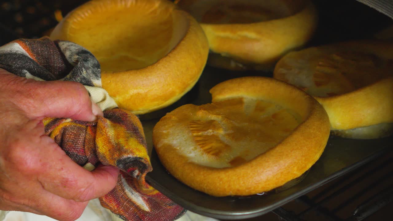 Beautifully Risen British Yorkshire Puddings Being Removed from Oven. Side Dish Traditionally Served with Roast Dinners on Sunday.