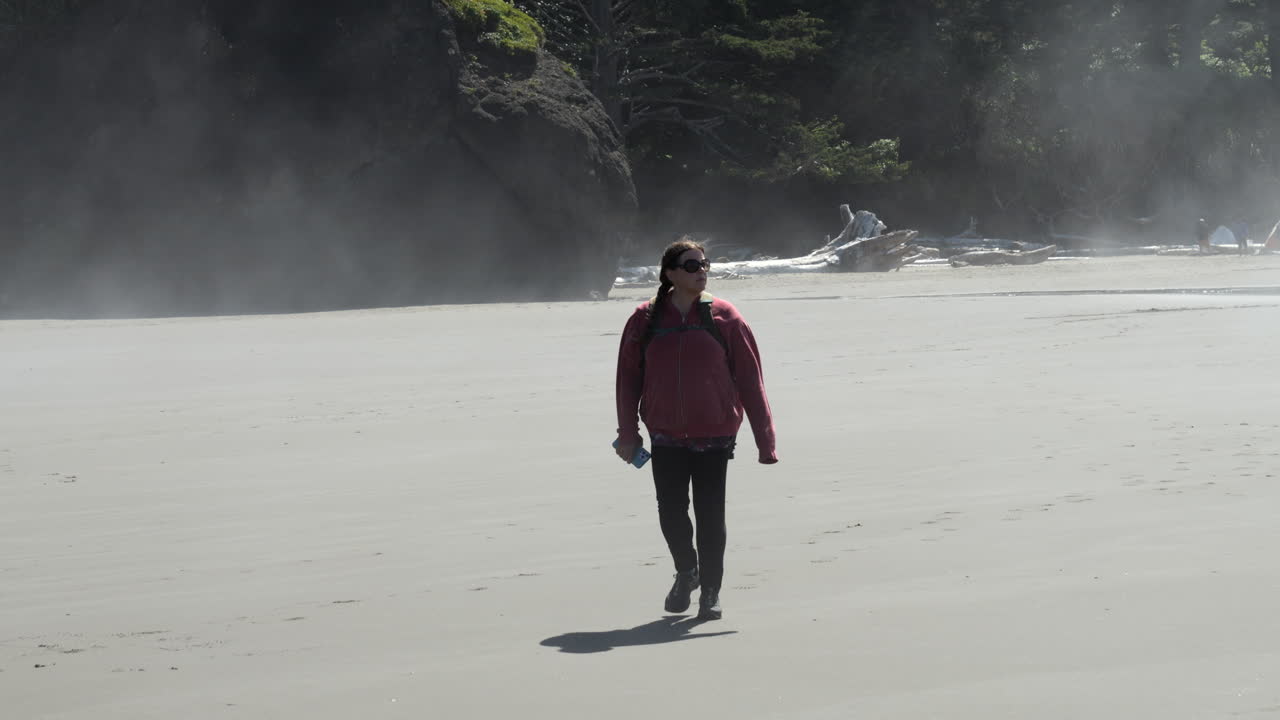 백그라운드에서 바위 형성과 해변에서 안개와 안개 속에서 걷는 빨간 재킷에 여자